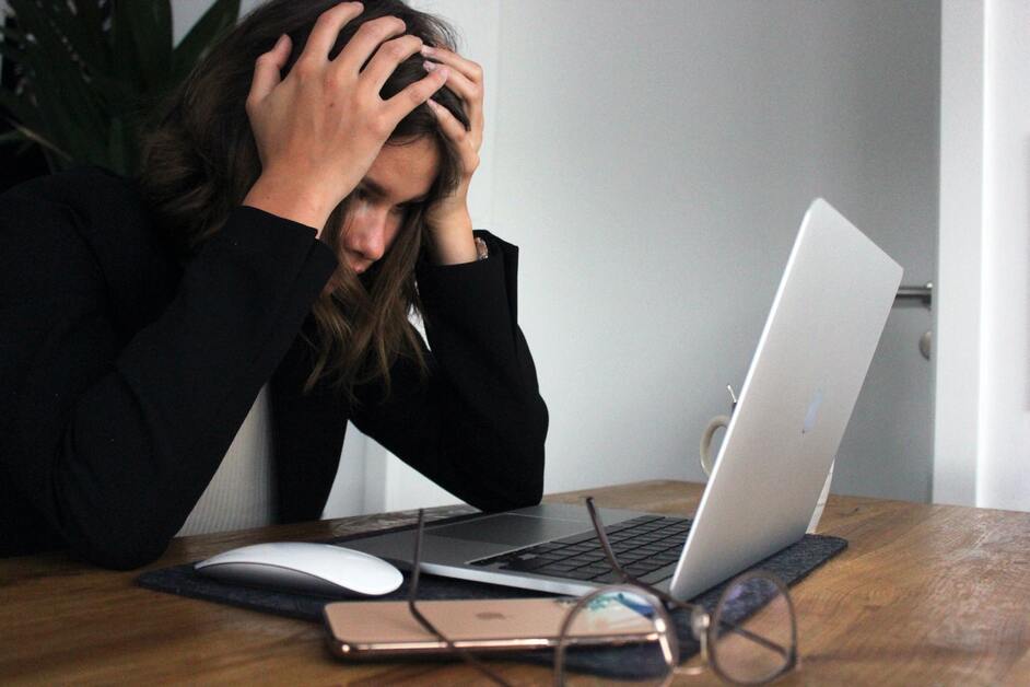 woman with head in hands in front of a laptop (workplace stress)